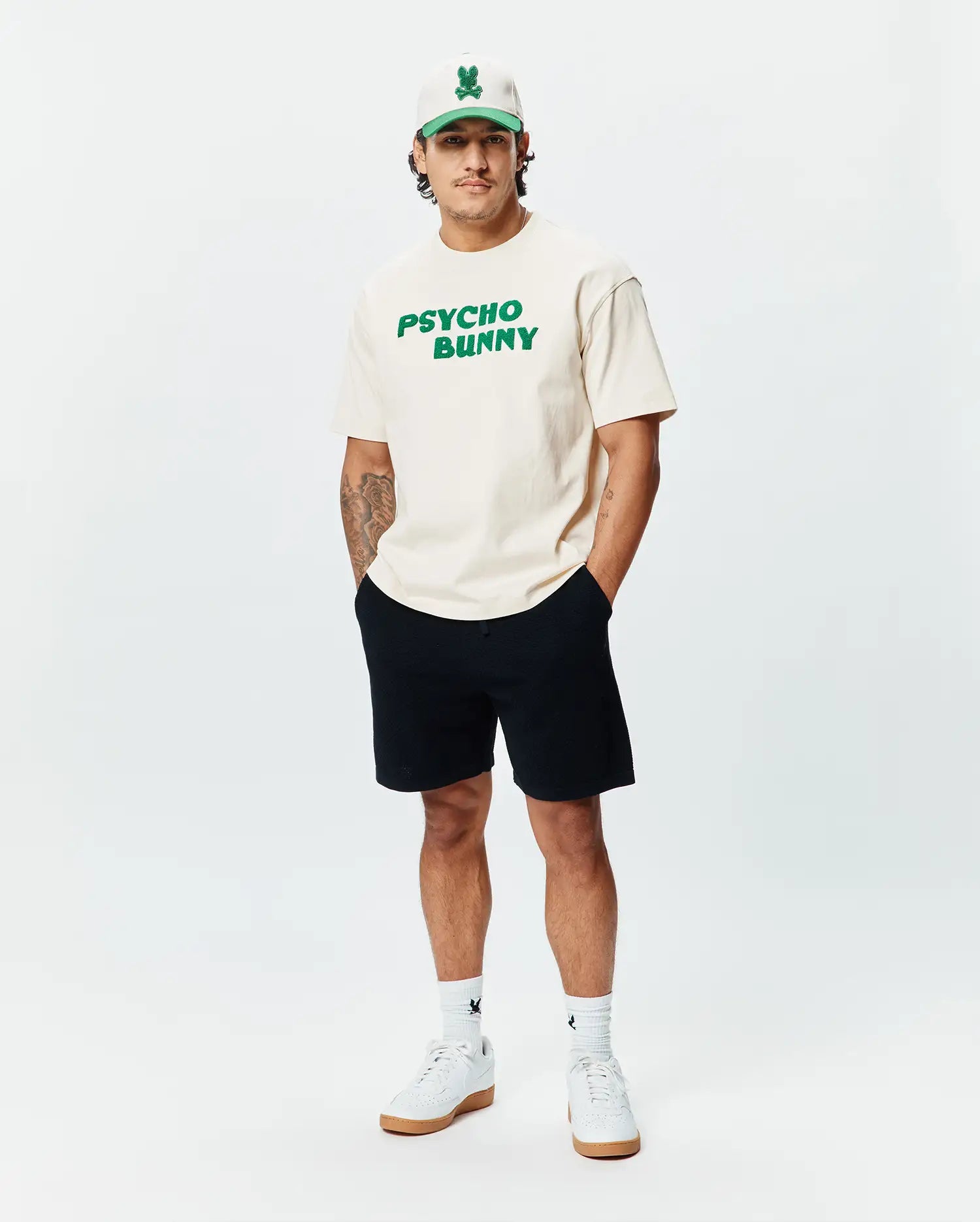 Cream Mens Craig Wordmark Tee, a relaxed fit jersey t-shirt featuring a large, bold green PSYCHO BUNNY wordmark graphic prominently displayed on the chest.