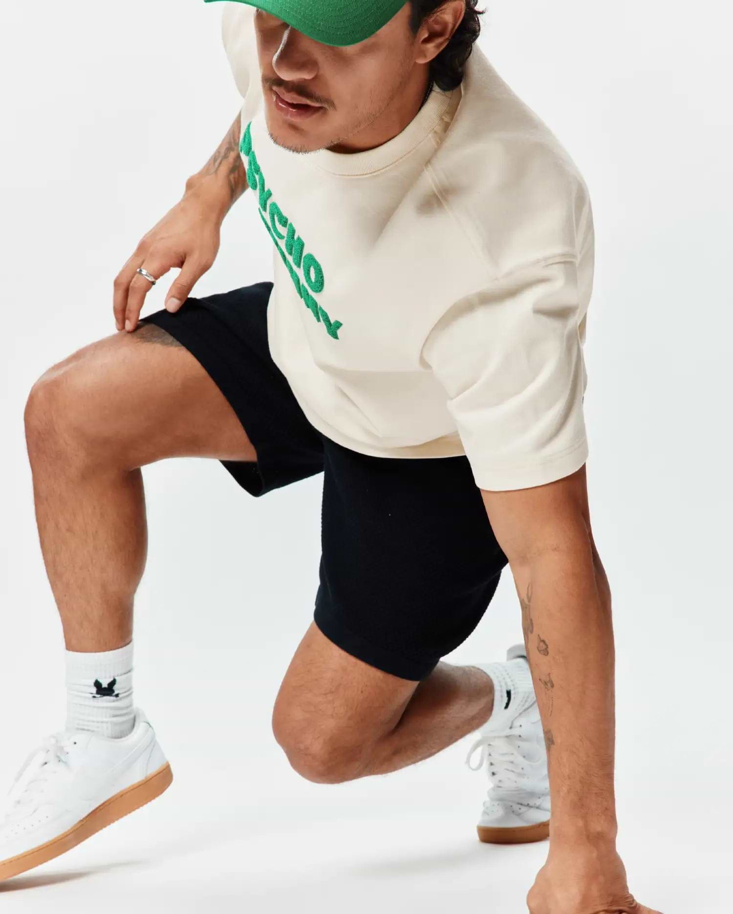 Mens Craig Wordmark Tee, an off-white jersey tee with a bold green PSYCHO chest logo, paired with black relaxed shorts and white socks featuring the iconic bunny skull.