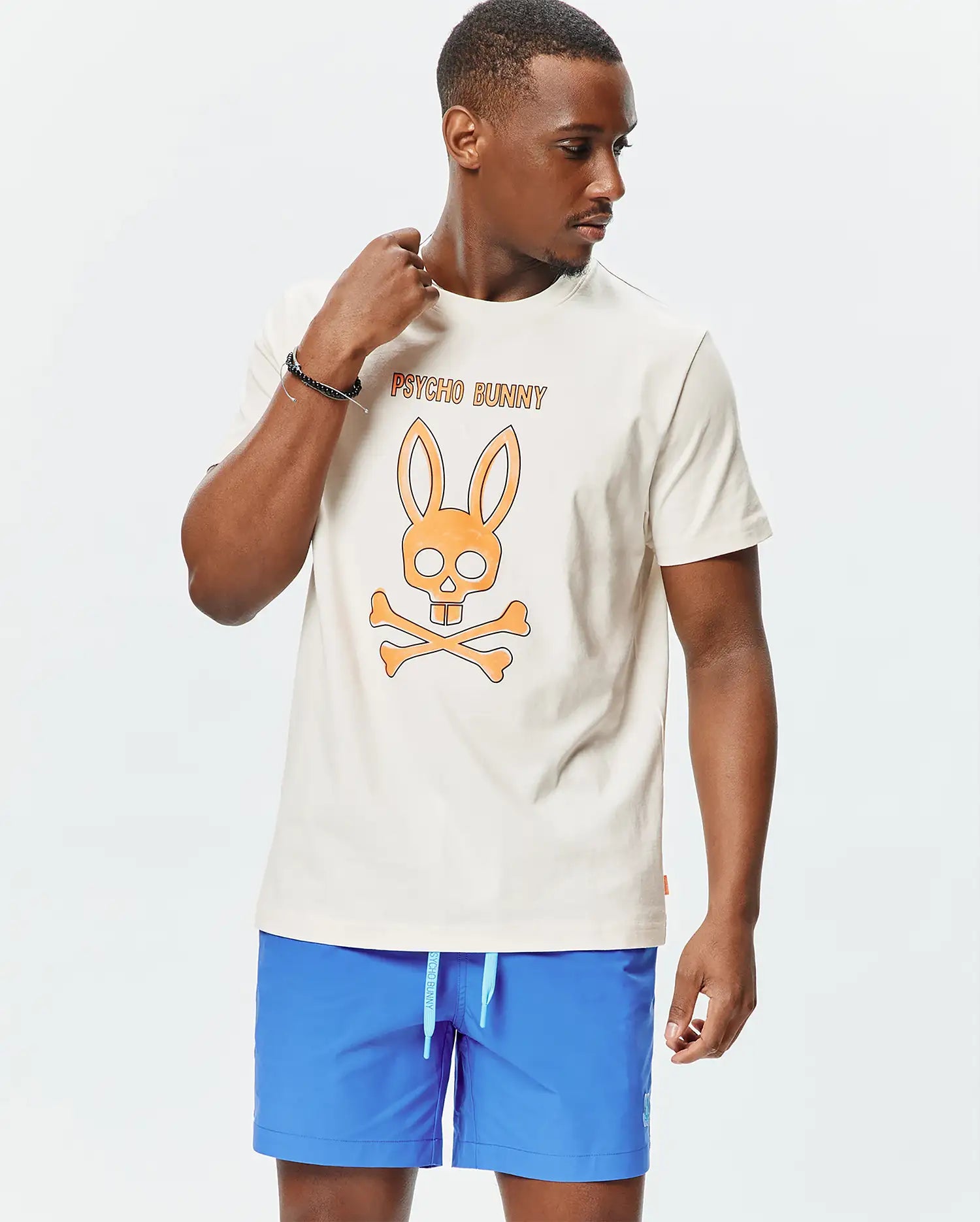 Mens Adler Graphic Tee, a cream classic fit jersey knit t-shirt featuring a large orange Psycho Bunny skull and crossbones graphic with Psycho Bunny text on the center chest.