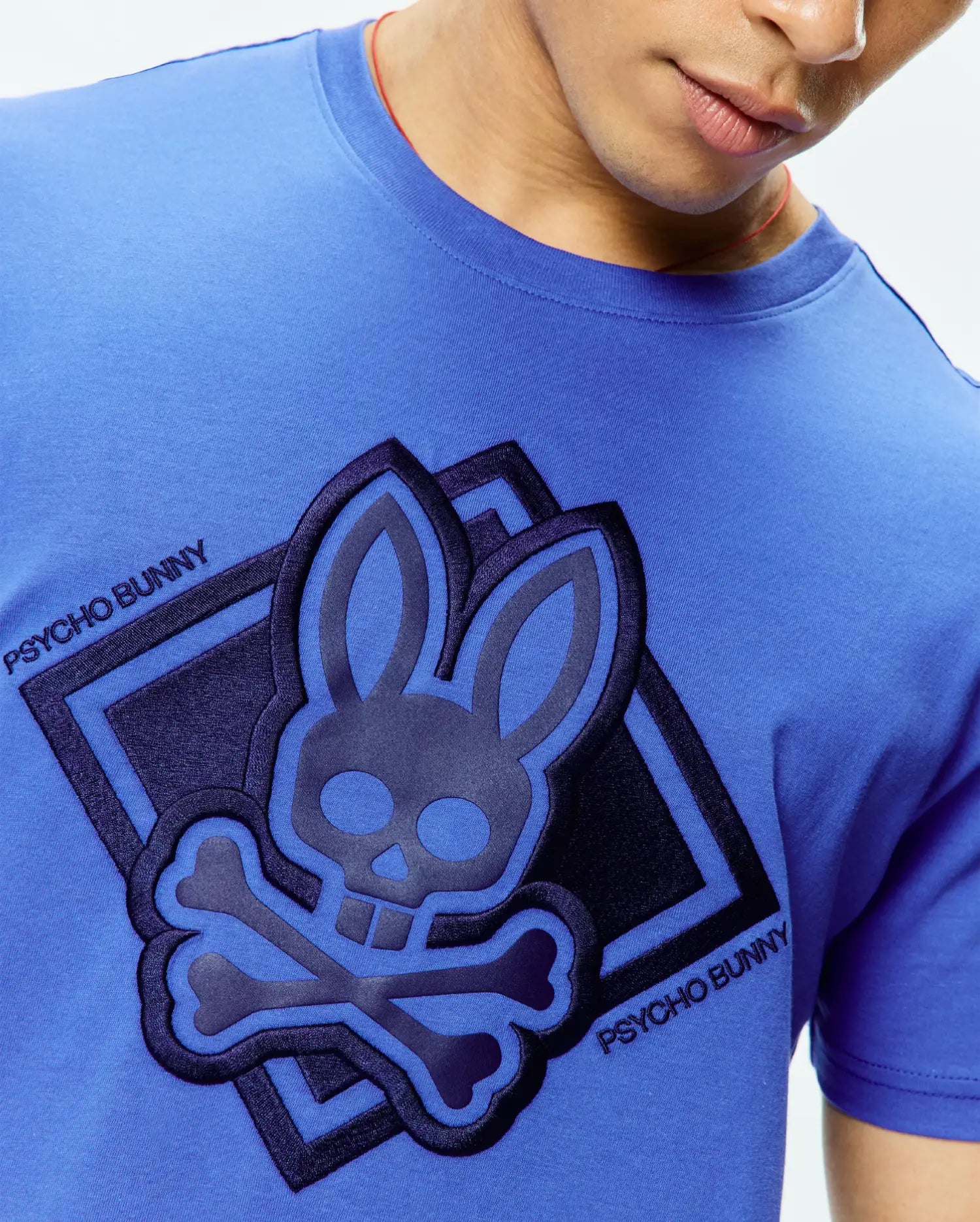 Mens Tobias Graphic Tee, a vibrant blue jersey t-shirt with a large, central raised Psycho Bunny skull logo in layered dark blue and black, set in a diamond graphic with diagonal Psycho Bunny text.
