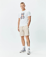 Mens Ethan Graphic Tee, a white classic fit jersey t-shirt featuring a large, colorful abstract Psycho Bunny skull graphic on the chest, paired with beige French terry drawstring shorts with a small embroidered bunny logo. (5)
