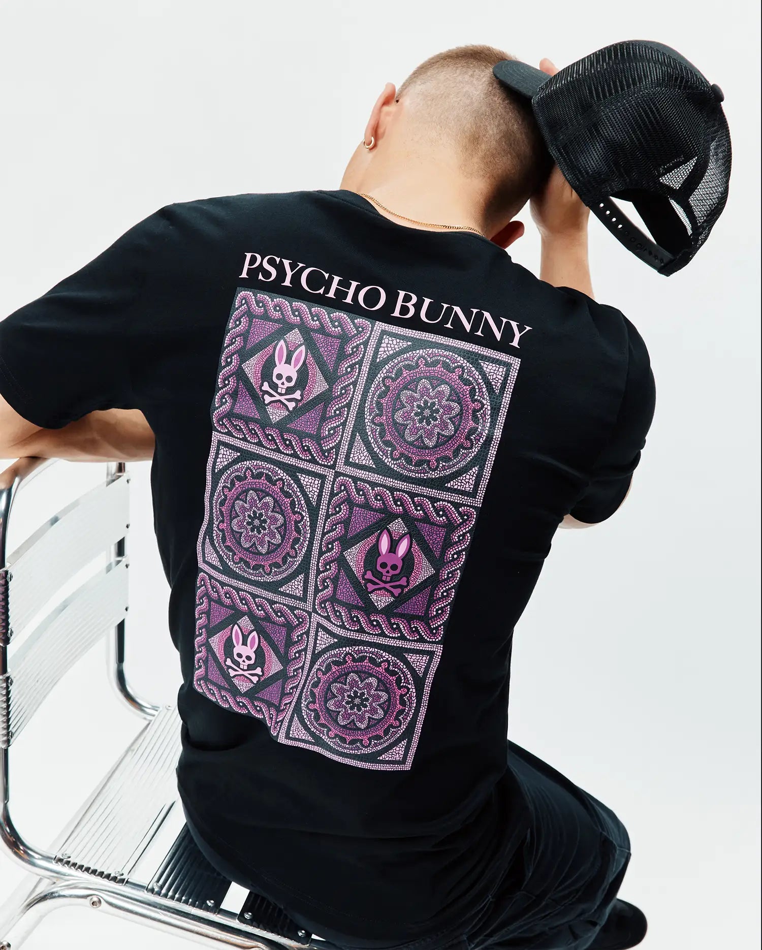 Mens Frank Back Graphic Tee, a black classic fit jersey t-shirt featuring a large back graphic with intricate pink and purple mandala patterns and multiple small Psycho Bunny skull logos, topped with pink PSYCHO BUNNY text.