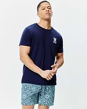 Mens Frank Back Graphic Tee, a classic fit navy blue jersey t-shirt with a small white embroidered Psycho Bunny skull logo on the left chest, paired with teal and blue patterned shorts featuring integrated bunny skull motifs.