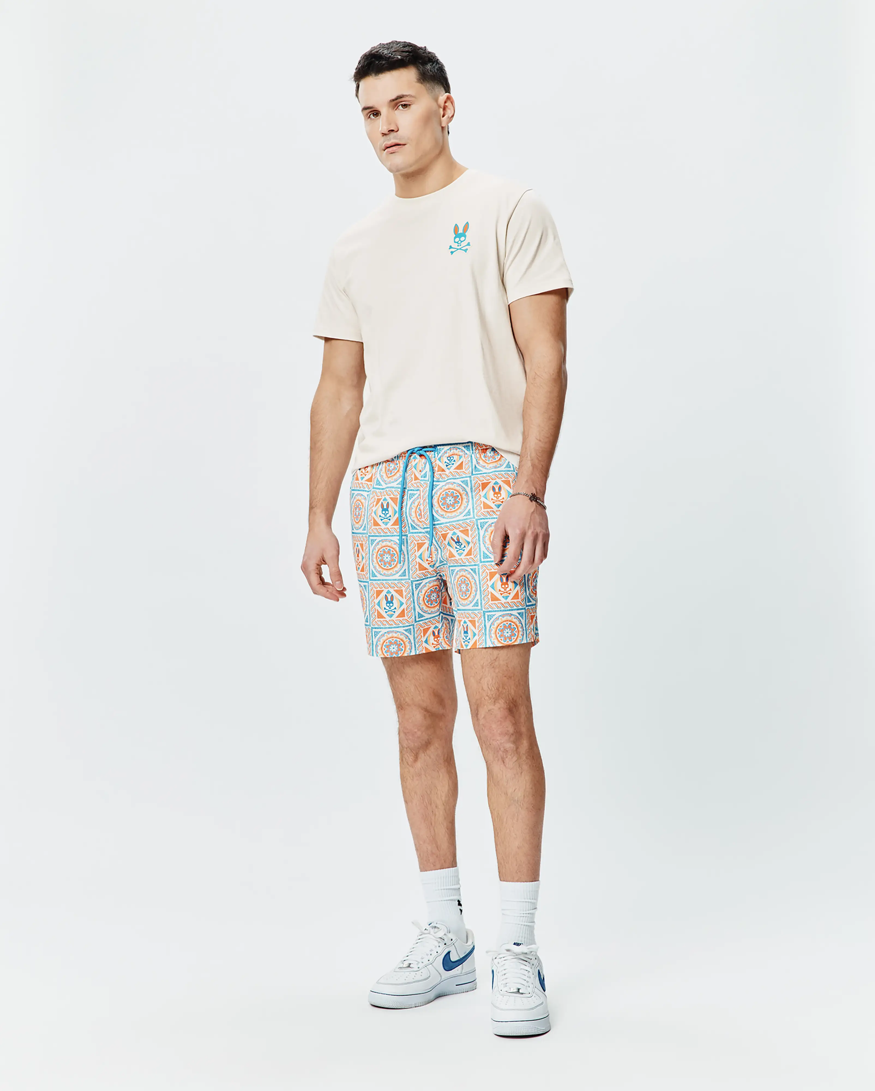 Mens Frank Back Graphic Tee, classic fit beige jersey with embroidered blue/orange Psycho Bunny skull chest logo. Relaxed shorts, all-over blue/orange geometric tile pattern, integrated bunny skull logos, blue drawstring. (5)