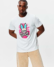 Mens Marcus Bunny Graphic Tee, a classic fit white jersey t-shirt featuring a large chest graphic of the Psycho Bunny skull with light blue ears on a pink paint splatter background, plus a small red hem tag.