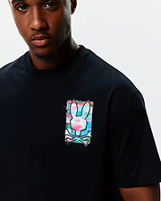 Mens Isaac Relaxed Fit Tee, black soft jersey with a relaxed fit, featuring a medium-sized left chest graphic of the Psycho Bunny skull logo in a vibrant pink, blue, and green paint splatter design.