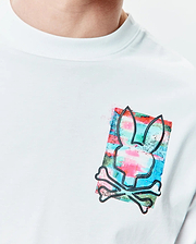 Mens Isaac Relaxed Fit Tee, a white smooth jersey tee with a medium left chest graphic of the Psycho Bunny skull outline over a vibrant pink, blue, and green watercolor splatter.