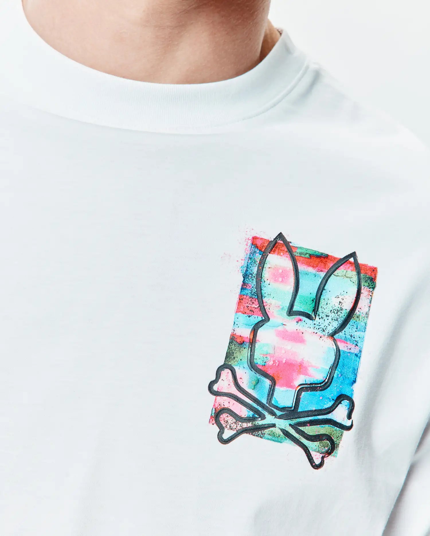 Mens Isaac Relaxed Fit Tee, a white smooth jersey tee with a medium left chest graphic of the Psycho Bunny skull outline over a vibrant pink, blue, and green watercolor splatter.
