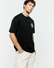 Mens Duncan Relaxed Fit Tee, black jersey knit with a relaxed fit, featuring a prominent pink and white Psycho Bunny skull and crossbones logo on the left chest.