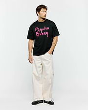 Mens Duncan Wordmark Relaxed Fit Tee, a black jersey t-shirt featuring a bold, large pink graffiti-style Psycho Bunny wordmark graphic with splatter details on the center chest.
