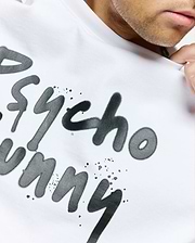 White Mens Duncan Wordmark Relaxed Fit Tee in soft jersey, featuring a large dark grey graffiti-style Psycho Bunny wordmark print with paint splatters on the chest.
