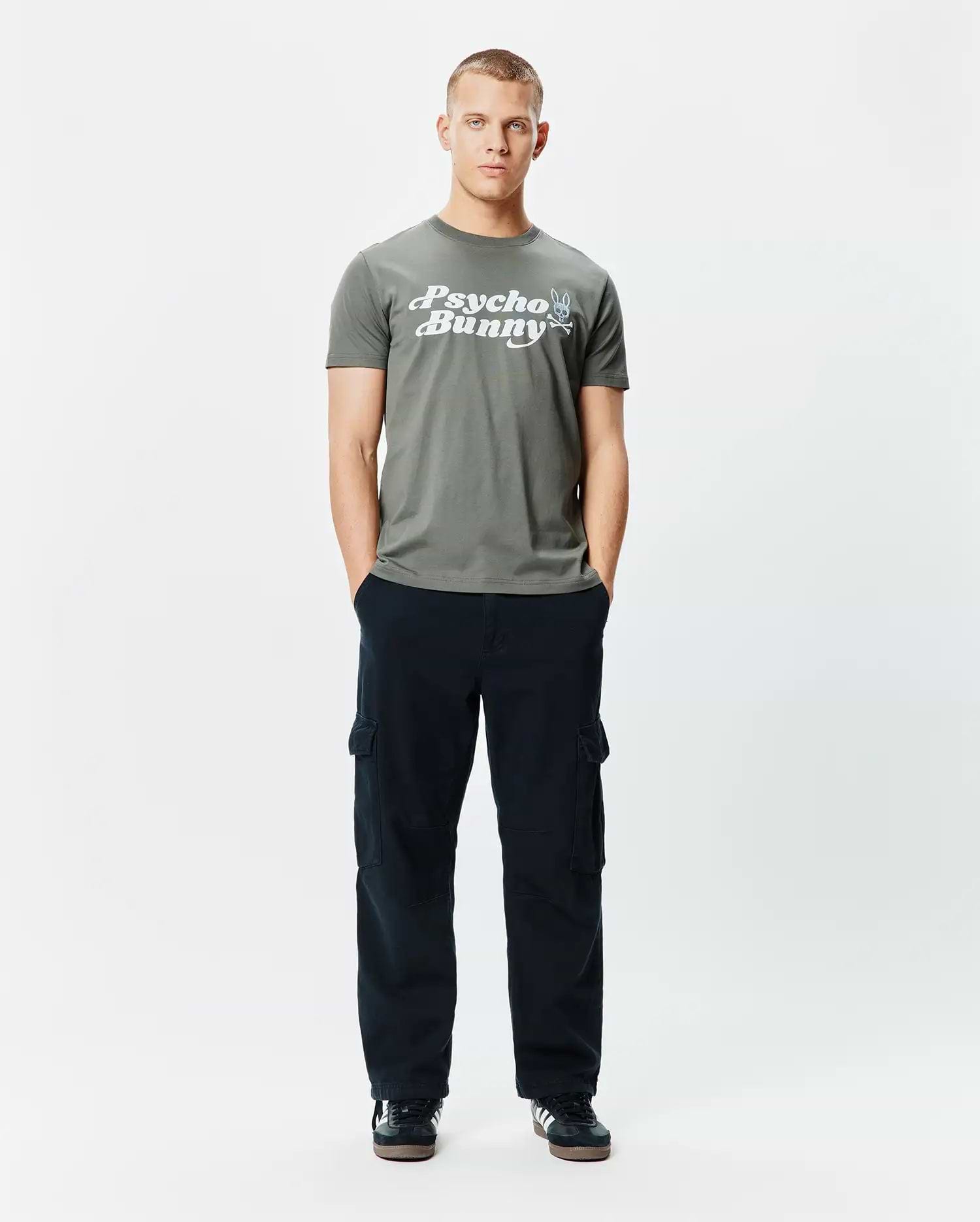 Mens Byron Wordmark Tee, a classic fit olive green jersey t-shirt with a large white Psycho Bunny wordmark graphic and blue-eyed skull logo on the chest.