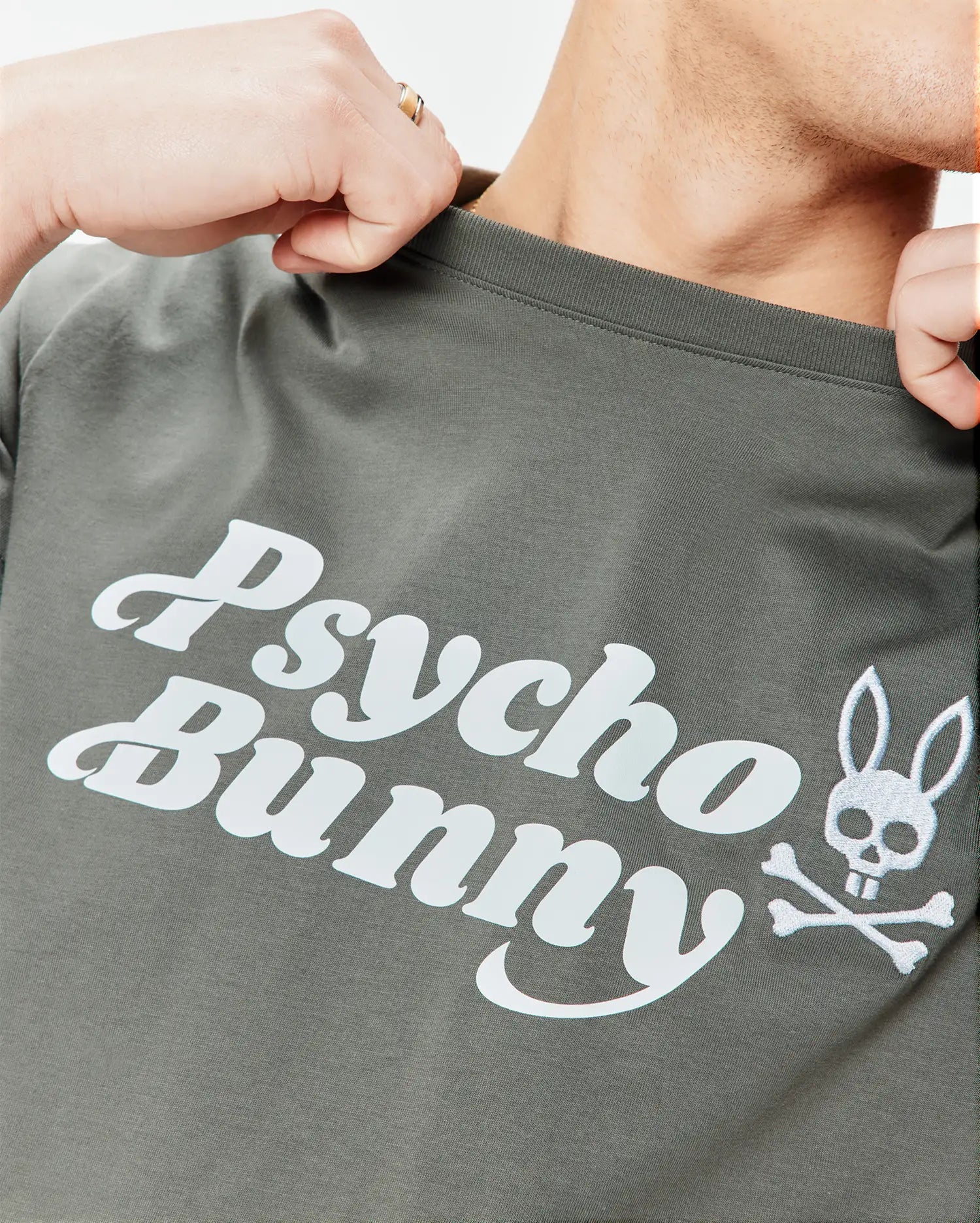 Mens Byron Wordmark Tee in dark olive green, a classic fit soft jersey knit t-shirt featuring a large white Psycho Bunny wordmark and embroidered bunny skull with crossbones graphic on the chest.