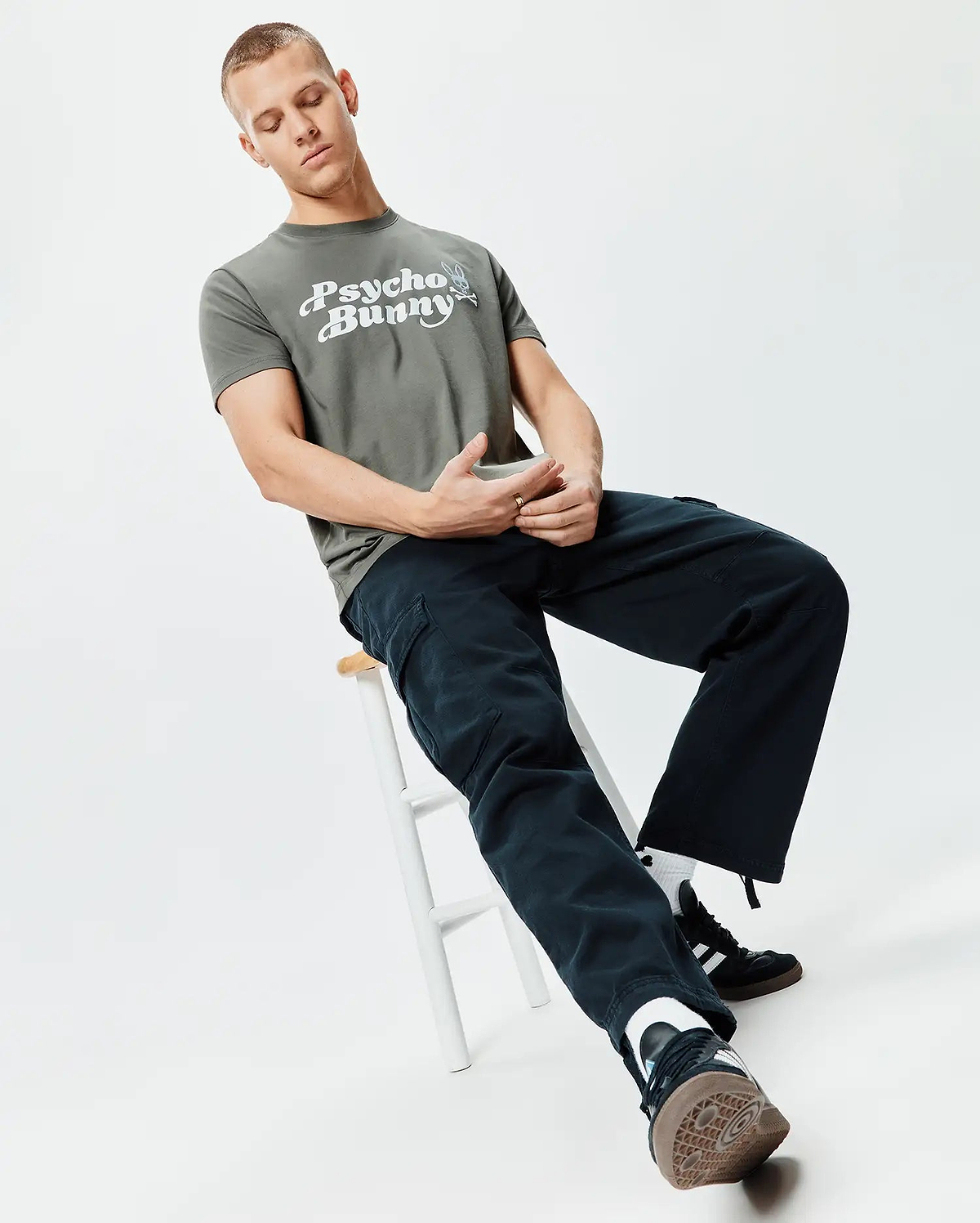 Mens Byron Wordmark Tee in muted olive green, a classic fit jersey tee. Features a large white Psycho Bunny wordmark with the iconic bunny skull logo printed prominently on the chest.