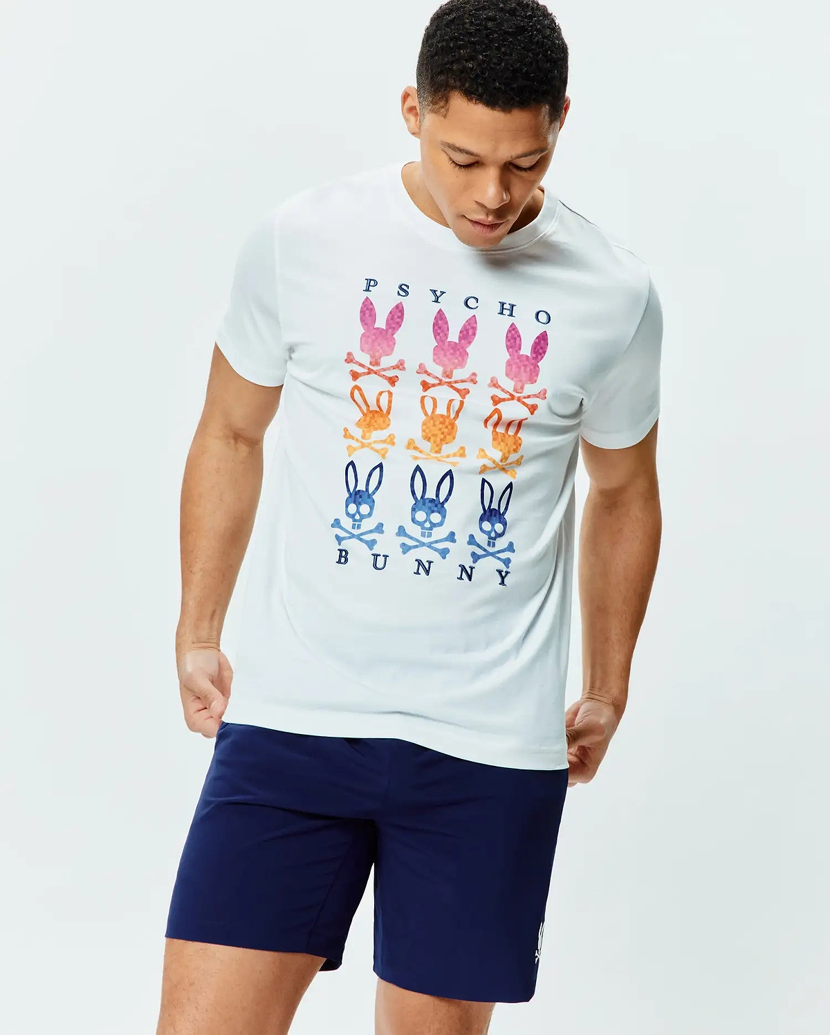 White Mens Colt Graphic Tee, a classic fit jersey t-shirt featuring a large central graphic of nine vibrant Psycho Bunny skull and crossbones logos in pink, orange, and blue, with PSYCHO BUNNY text.