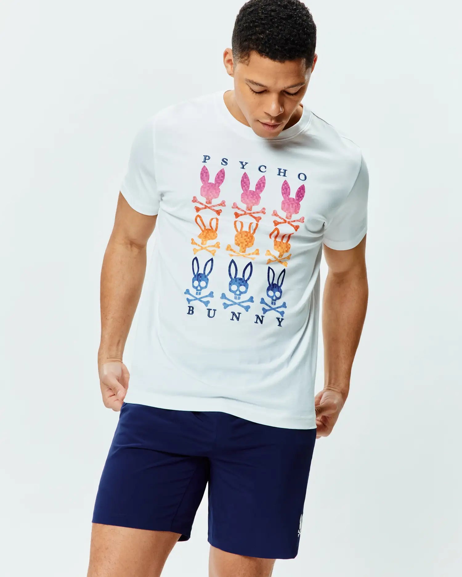 White Mens Colt Graphic Tee, a classic fit jersey t-shirt featuring a large central graphic of nine vibrant Psycho Bunny skull and crossbones logos in pink, orange, and blue, with PSYCHO BUNNY text.