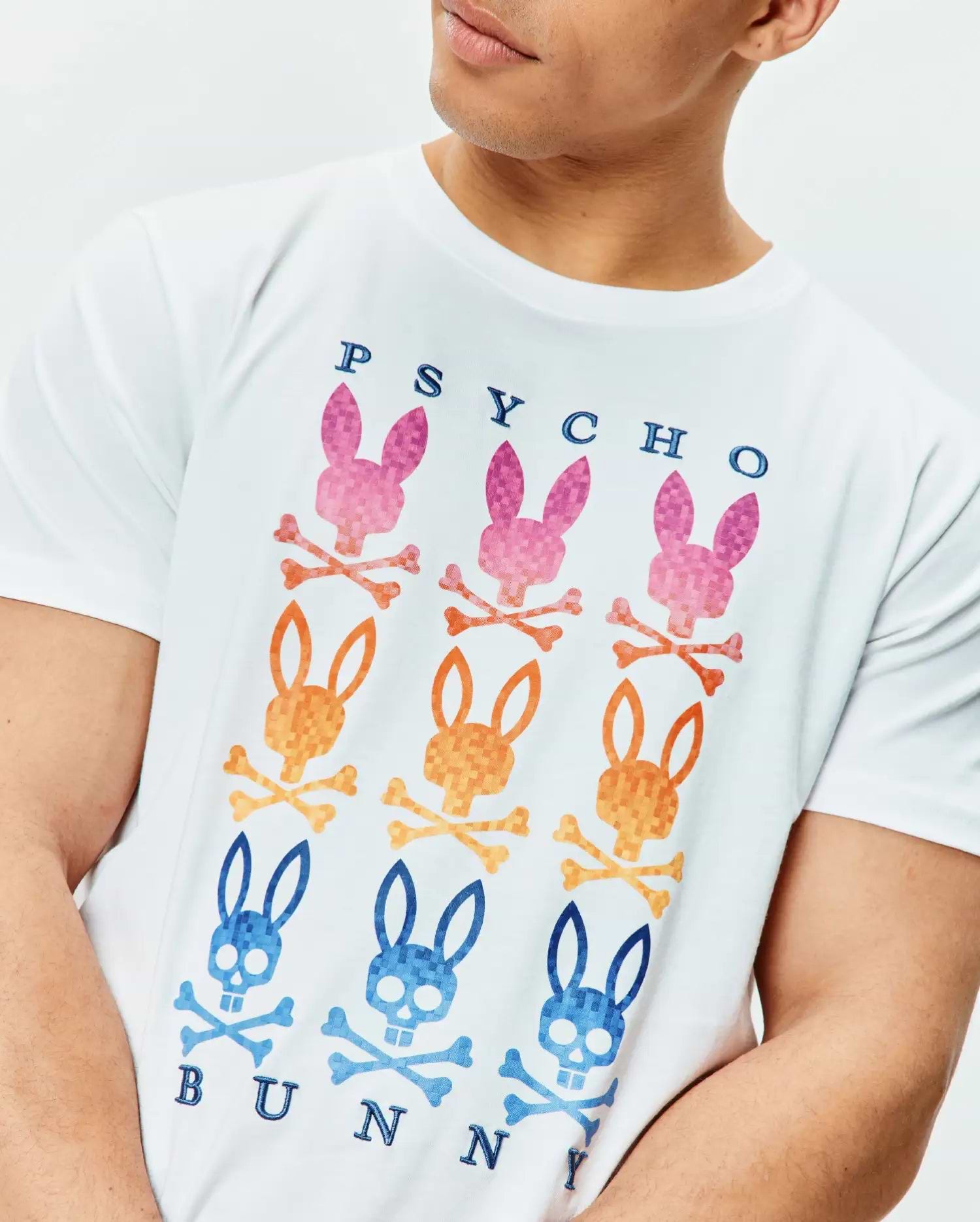 Mens Colt Graphic Tee, white classic fit jersey knit with a large chest graphic of nine gradient pink, orange, and blue Psycho Bunny skull logos and dark blue text.