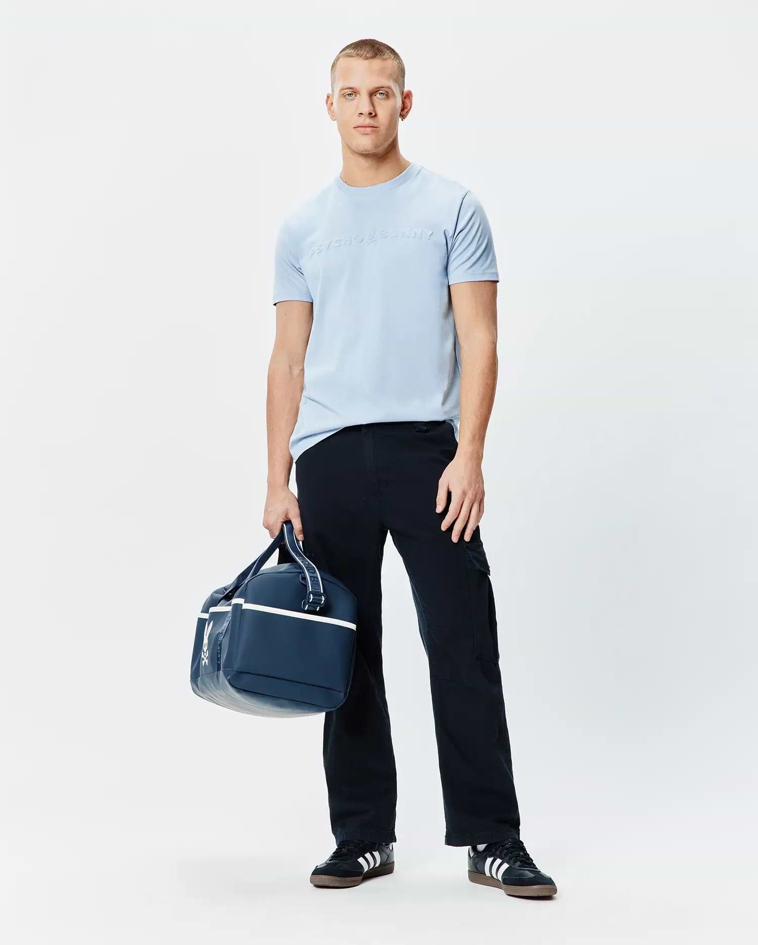 Mens Royce Graphic Tee, a light blue classic fit jersey t-shirt featuring a large, subtle tone-on-tone embossed Psycho Bunny text logo prominently centered on the chest.
