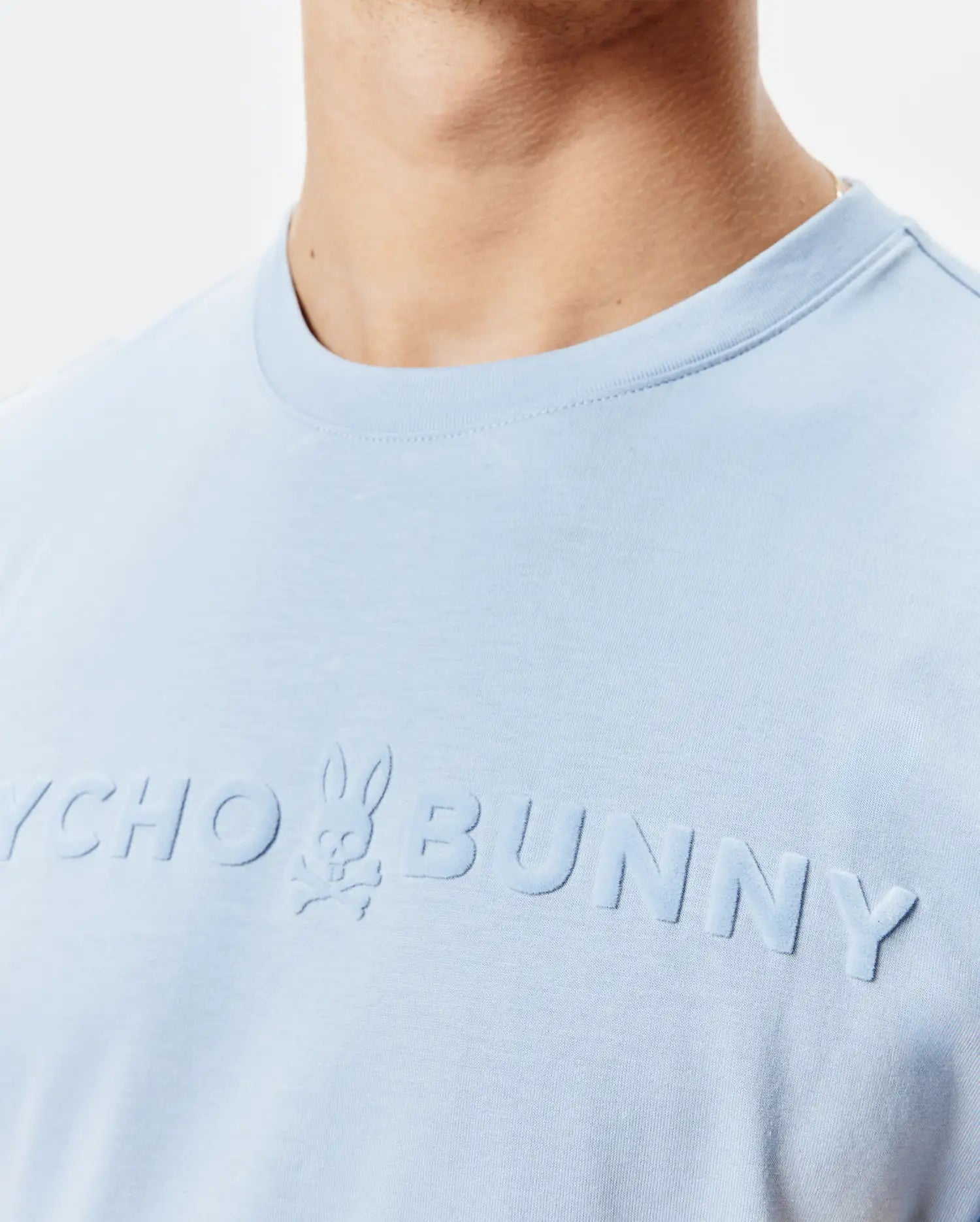 Mens Royce Graphic Tee, a light blue classic fit jersey t-shirt featuring a large, embossed, tone-on-tone Psycho Bunny logo with skull graphic on the chest.