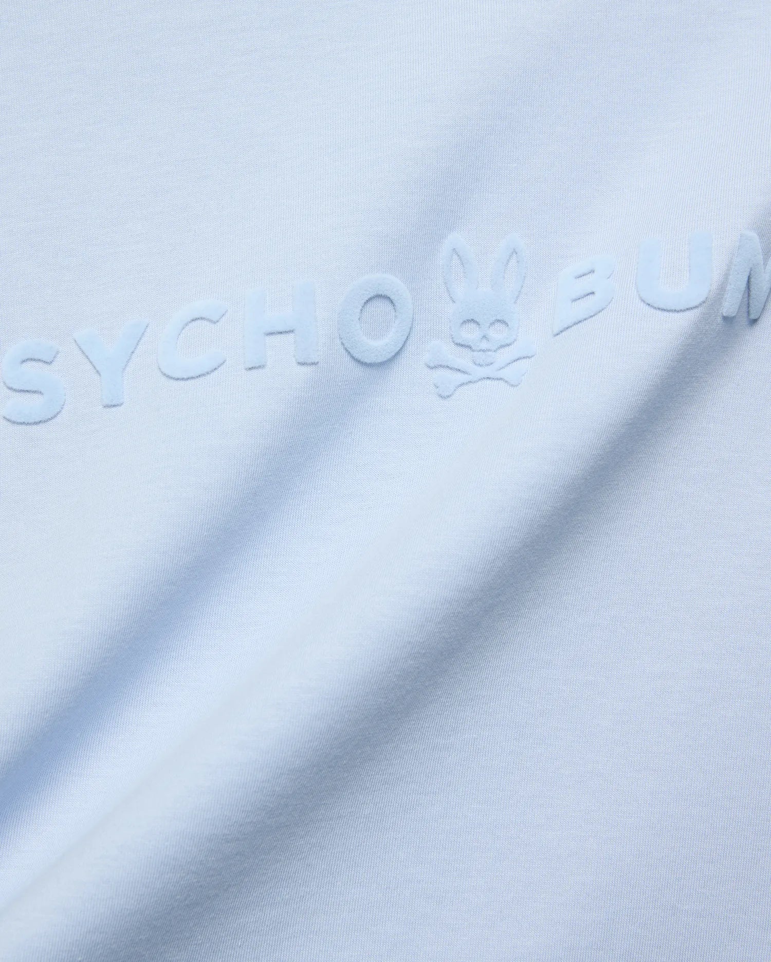 Mens Royce Graphic Tee, light blue jersey knit, featuring a large, tonal, raised velvety Psycho Bunny text logo with the iconic bunny skull on the chest.