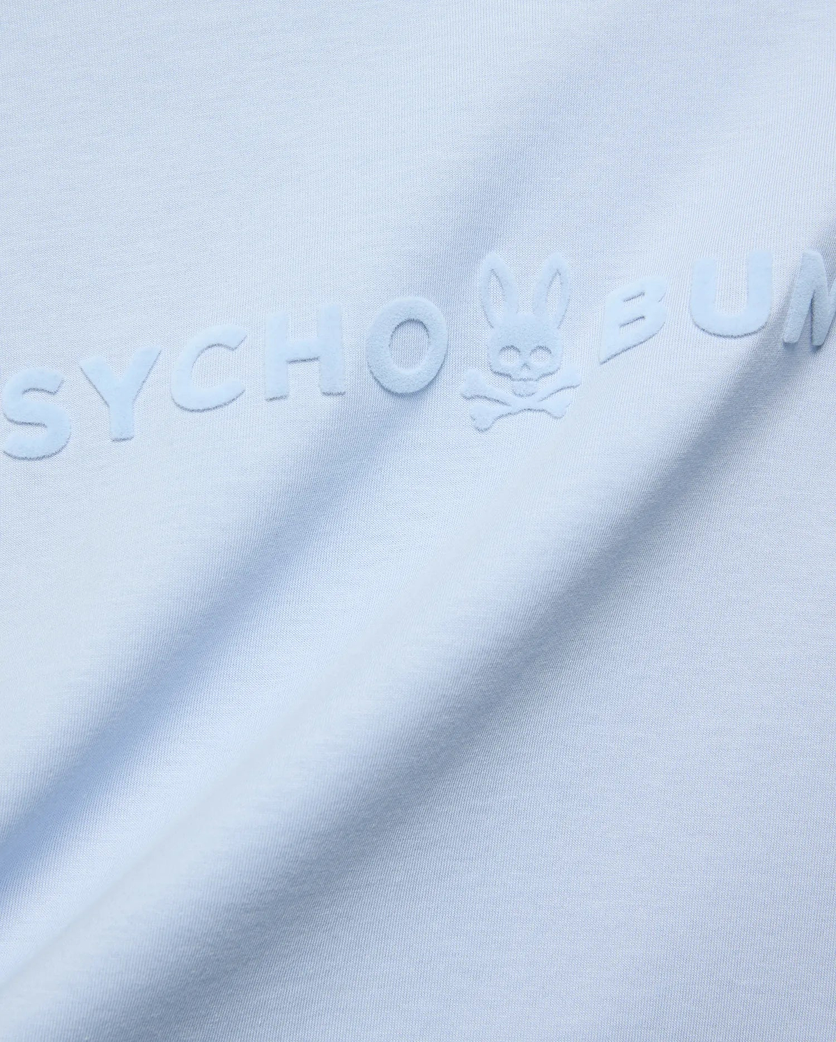 Mens Royce Graphic Tee, light blue jersey knit, featuring a large, tonal, raised velvety Psycho Bunny text logo with the iconic bunny skull on the chest.