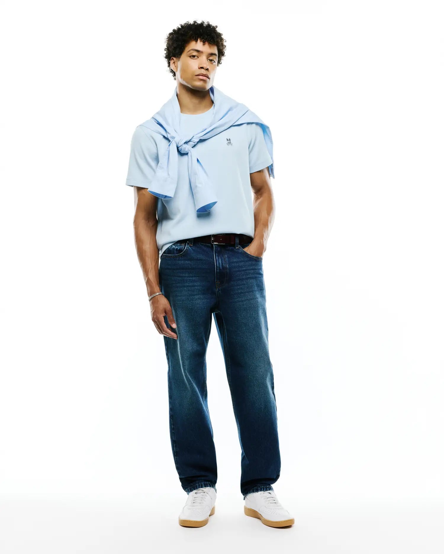 Light blue Mens Maxton Waffle Tee featuring a small embroidered Psycho Bunny skull logo on the left chest, styled with dark wash denim jeans and a light blue sweater.