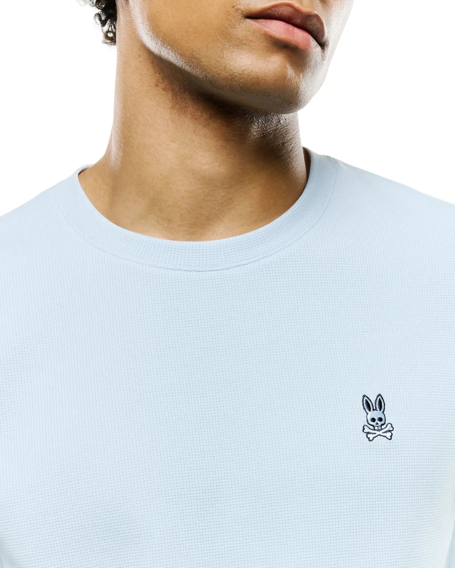 Mens Maxton Waffle Tee, a light blue classic fit crewneck with a textured waffle knit fabric, featuring a small embroidered black and white Psycho Bunny skull logo on the left chest.