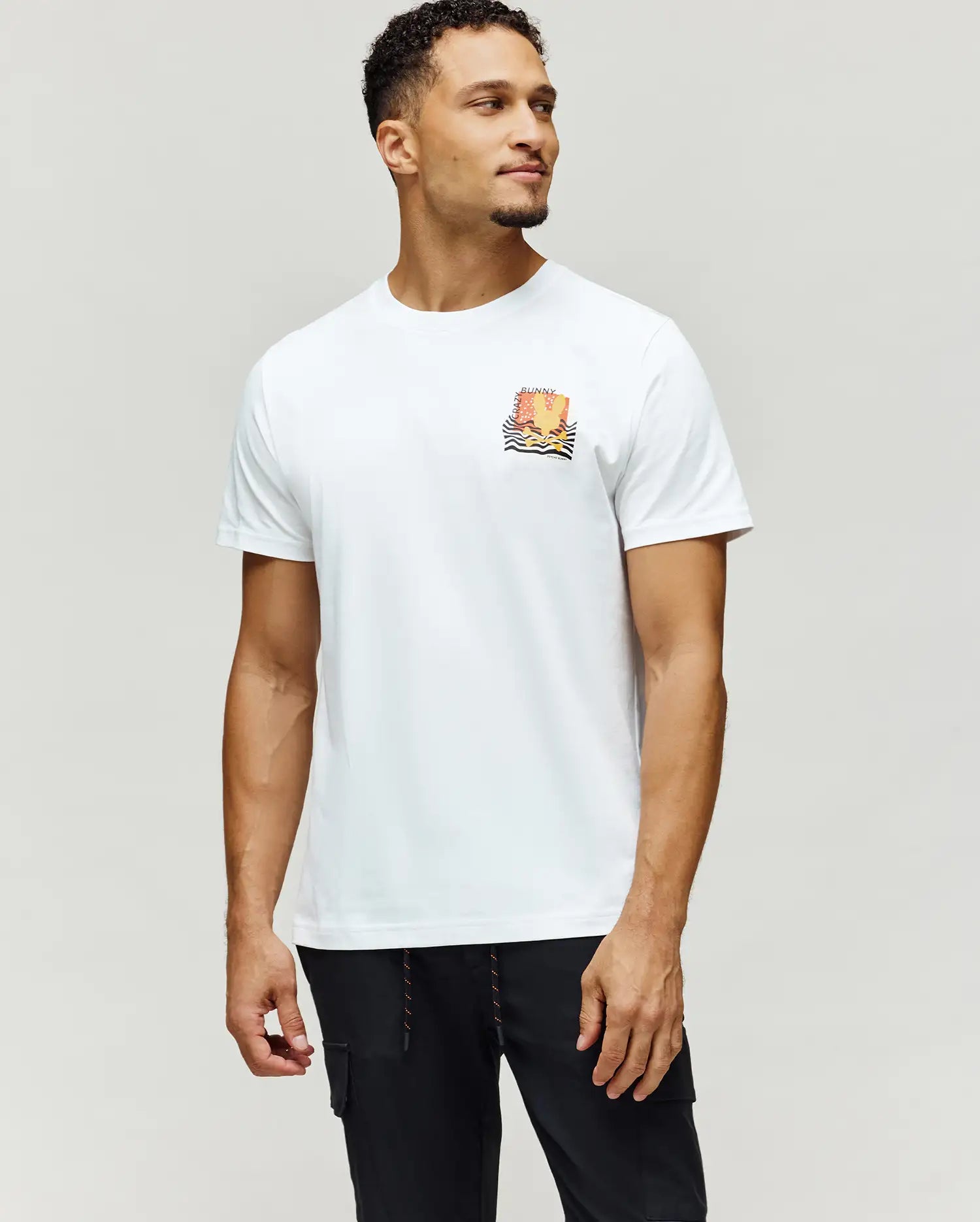 Mens Crazy Bunny Graphic Tee, a classic fit white jersey knit t-shirt with a small, colorful orange, yellow, and black graphic on the left chest, featuring CRAZY BUNNY text and wavy lines.