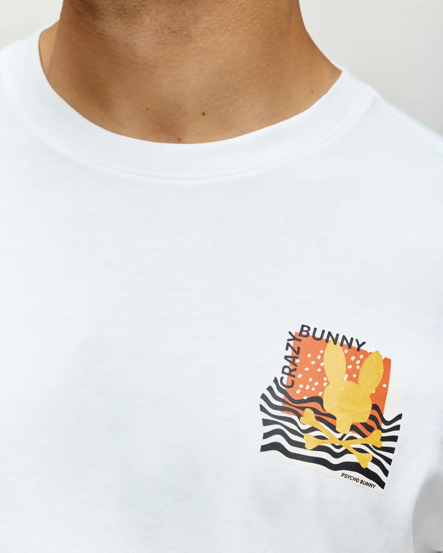 Mens Crazy Bunny Graphic Tee, a classic fit white jersey knit t-shirt with a vibrant left chest graphic featuring a yellow bunny skull, orange background, black wavy stripes, and Crazy Bunny text.