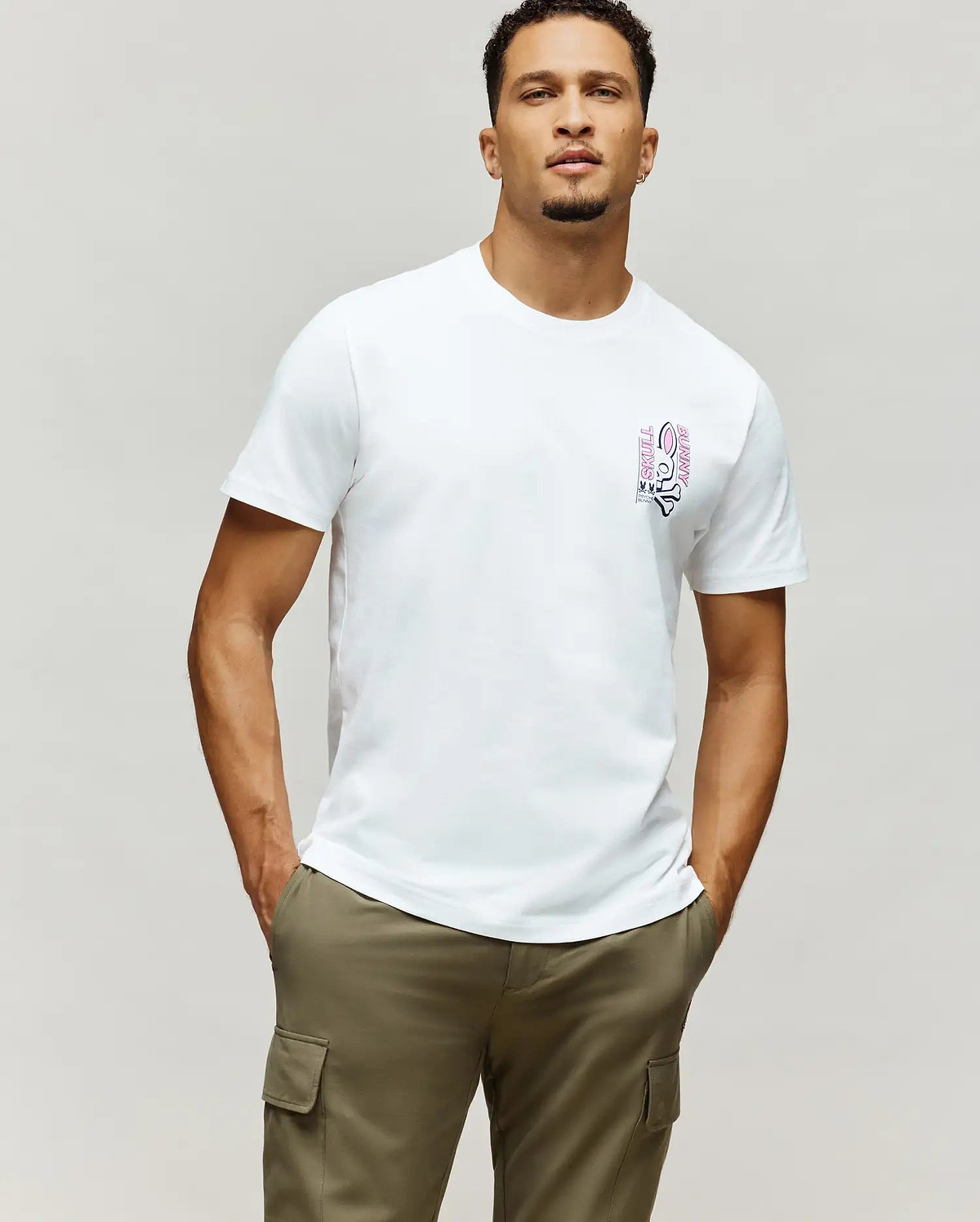 Mens Skull Bunny Graphic Tee: White classic fit jersey t-shirt featuring a vertical pink and black Psycho Bunny skull graphic with SKULL BUNNY text on the left chest.