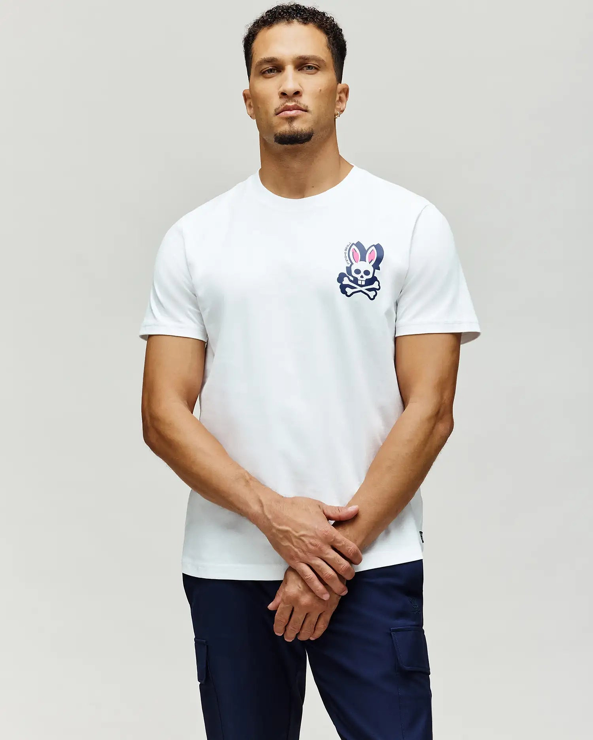 White classic fit jersey t-shirt with a navy blue and pink Psycho Bunny skull and crossbones graphic on the left chest, featuring PSYCHO BUNNY SKULL text. MENS PSYCHO SKULL GRAPHIC TEE.