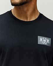 Mens Jarvis Chest Graphic Tee, a black classic fit premium jersey knit with a bold rectangular chest patch featuring three white Psycho Bunny skull and crossbones logos.