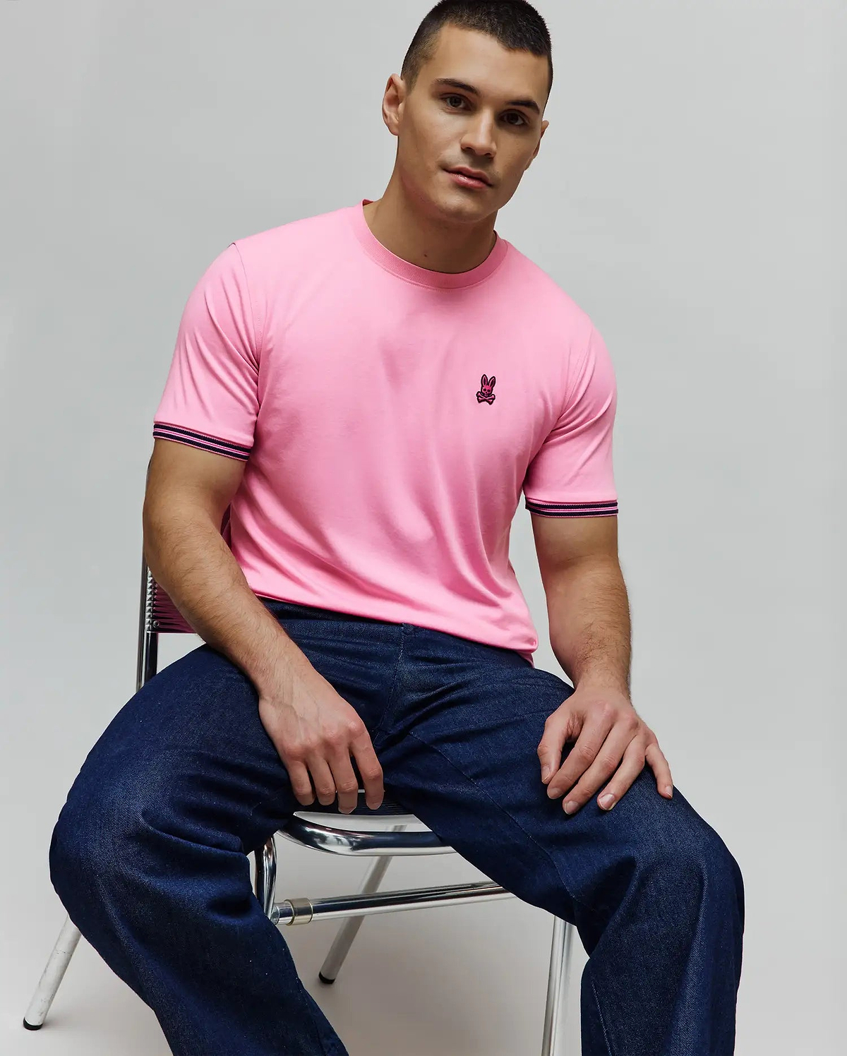 Mens Clark Performance Tee, a classic fit pink jersey t-shirt featuring a small embroidered dark pink Psycho Bunny skull logo on the left chest and striped dark blue and pink cuffs.