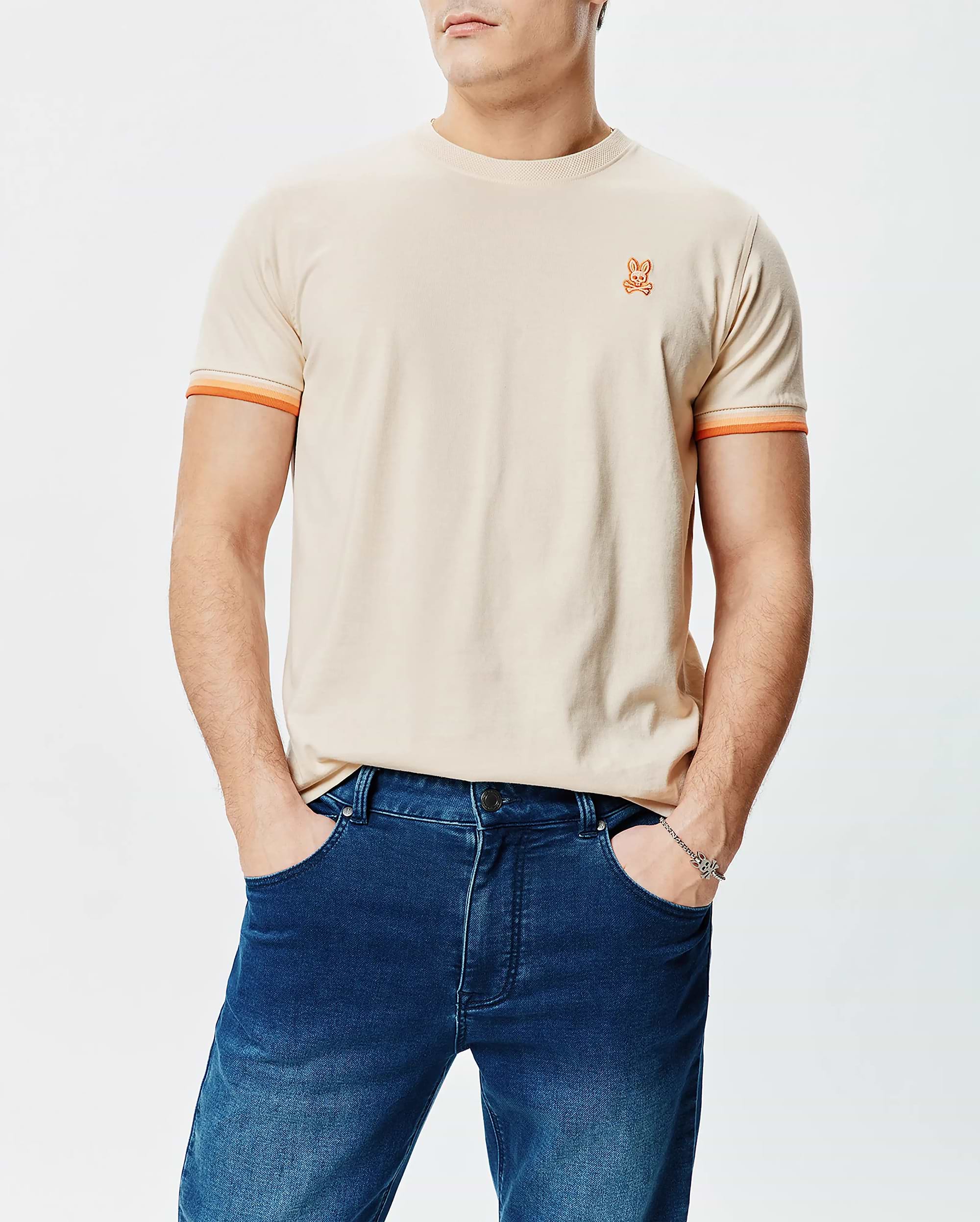 Mens Holden Tee, classic fit, beige jersey with small embroidered orange Psycho Bunny skull logo on left chest and orange striped sleeve cuffs.