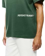Mens Haiden Relaxed Heavy Weight Tee in dark green heavyweight jersey, featuring a large white embroidered Psycho Bunny text logo on the chest, paired with white textured shorts displaying a small bunny skull logo. (2)