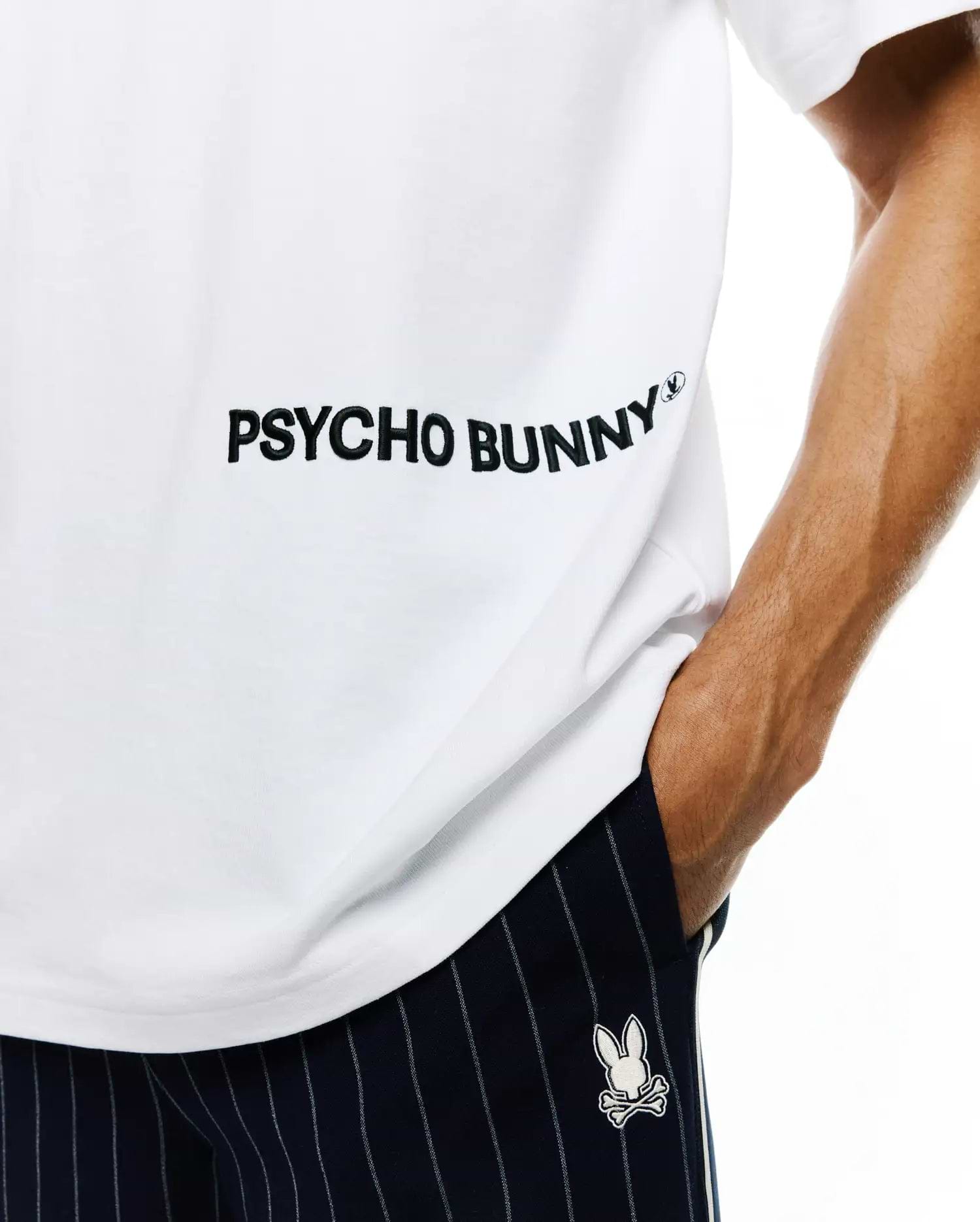 Mens Haiden Relaxed Heavy Weight Tee in white jersey with large black PSYCHO BUNNY text and small bunny skull logo, paired with navy pinstripe shorts featuring an embroidered white bunny skull.
