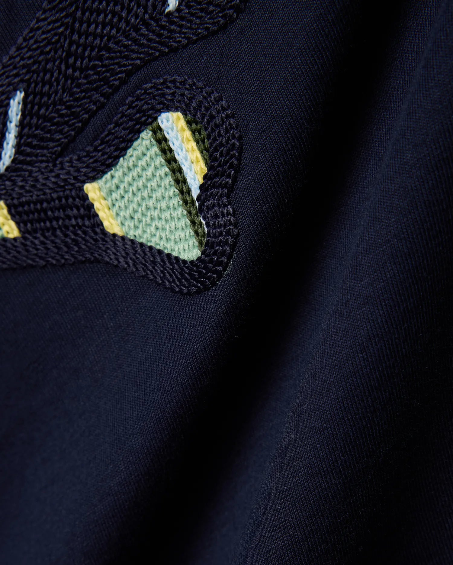 Mens Drew Embroidered Graphic Tee, a dark navy jersey knit with a prominent, textured Psycho Bunny skull logo detail featuring light blue, yellow, and green stripes.