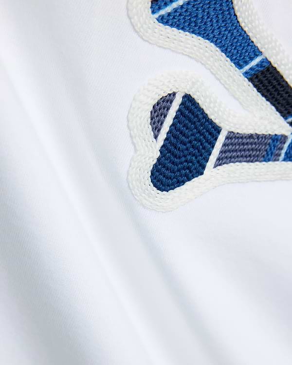 Mens Drew Embroidered Graphic Tee, white jersey knit, featuring a large Psycho Bunny graphic with blue, dark blue, and grey plaid-like embroidery outlined in white.