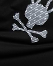 Mens Jaden Appliqué Graphic Tee. Black jersey with large grey and white Psycho Bunny skull and crossbones appliqué, featuring a repeating pattern of small white bunny skulls and chevron stripes.