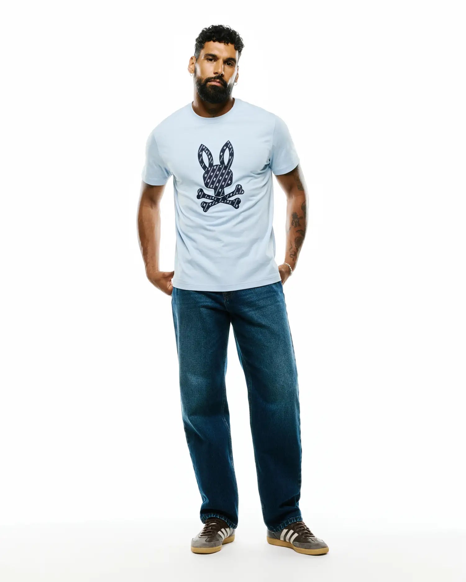 Mens Jaden Appliqué Graphic Tee, a light blue classic fit jersey t-shirt featuring a large central navy and white patterned Psycho Bunny skull and crossbones logo.