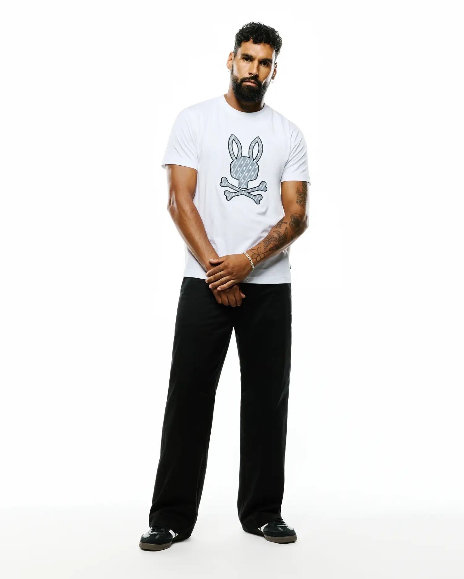 Mens Jaden Appliqué Graphic Tee, a white classic fit soft jersey t-shirt featuring a large center chest Psycho Bunny skull logo with a repeating bunny pattern and crossed bones.