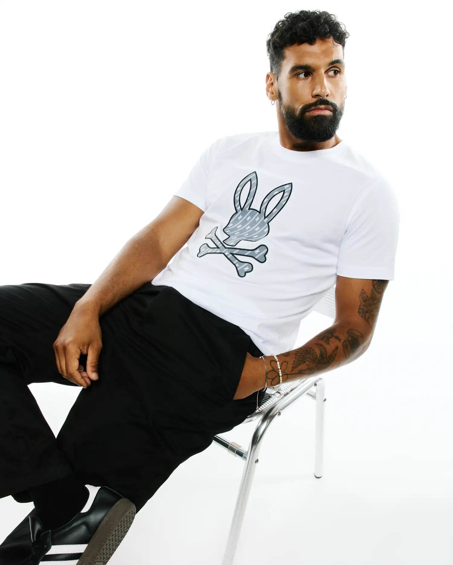 Mens Jaden Applique Graphic Tee, a classic fit white jersey t-shirt featuring a large grey and black Psycho Bunny skull and crossbones logo with a mini bunny skull pattern on the chest.