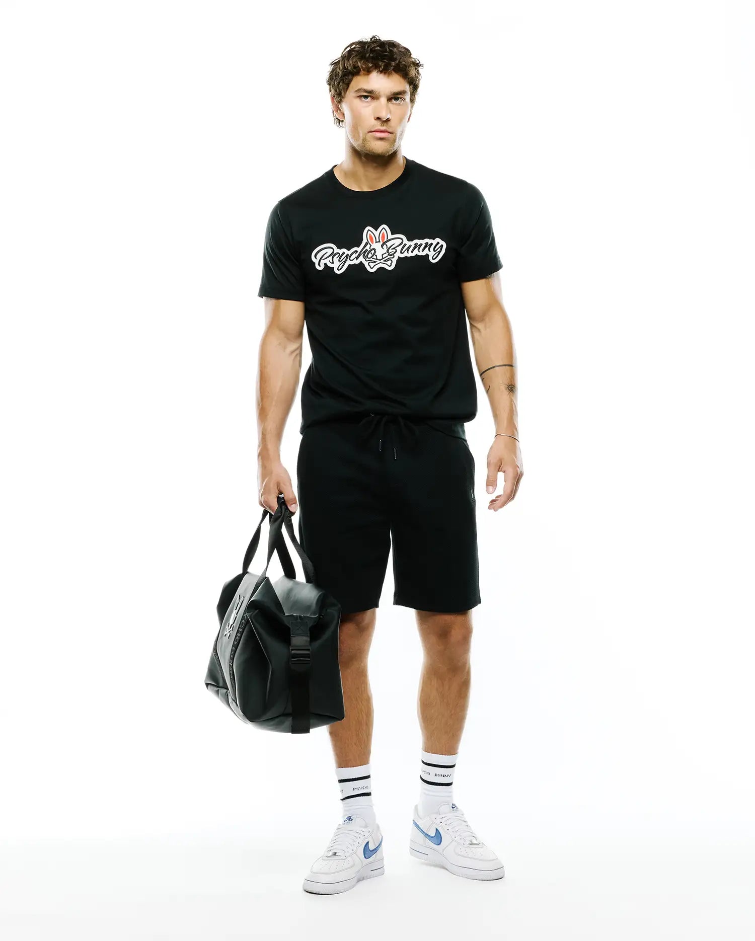 Black MENS JAYDON WORDMARK GRAPHIC TEE in a classic fit, crafted from soft jersey fabric, featuring a large white Psycho Bunny wordmark logo with red ears and blue eyes centered on the chest.