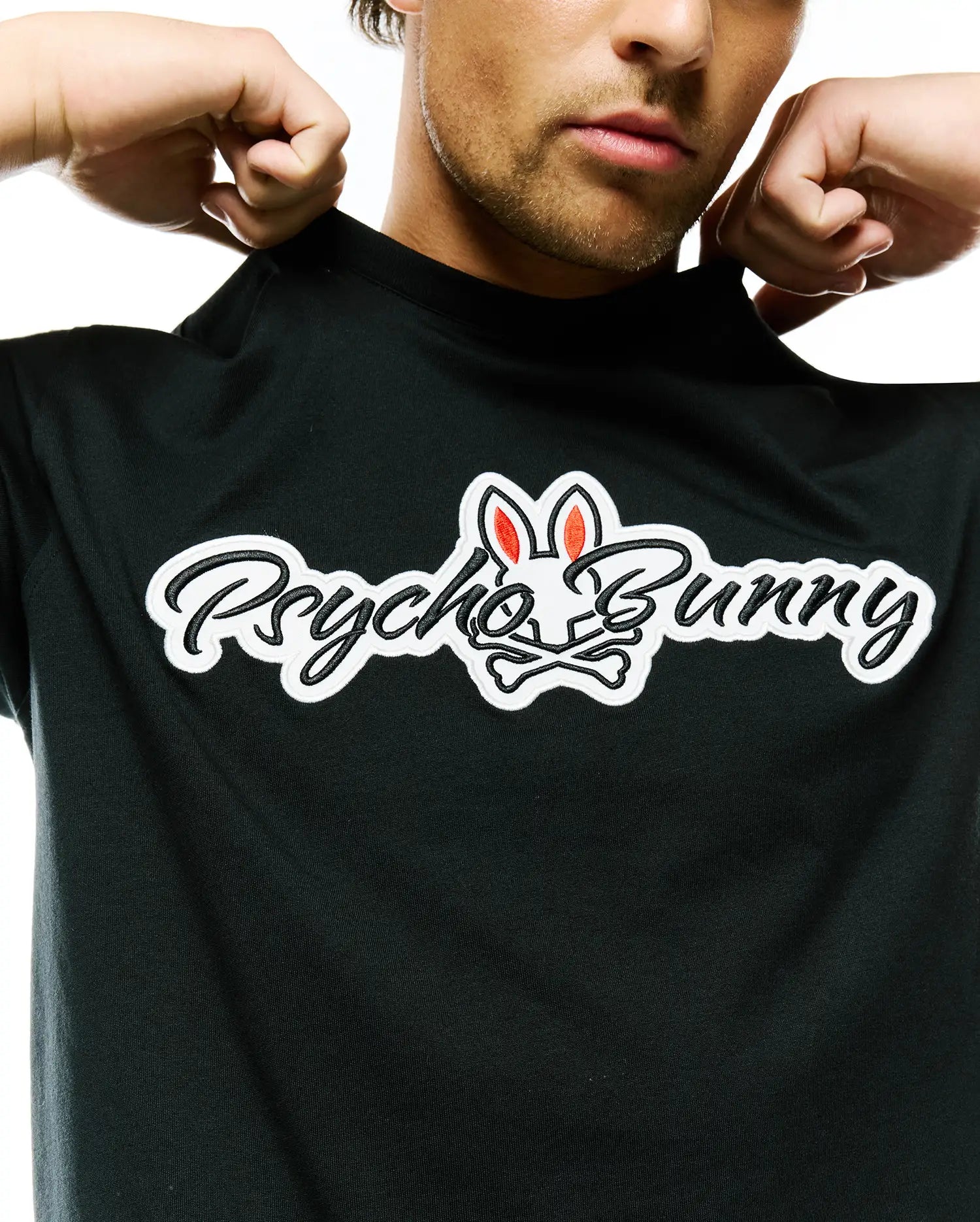 Mens Jaydon Wordmark Graphic Tee, black jersey knit, with a large center chest graphic: black script Psycho Bunny wordmark with white outline, and the iconic bunny skull logo with red inner ears and crossbones.