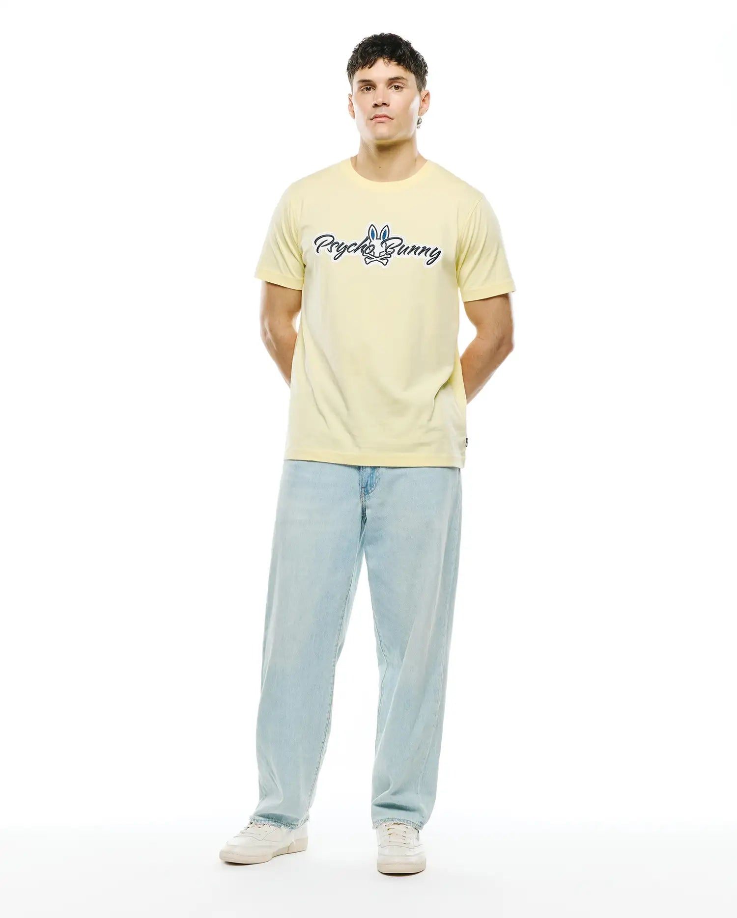 Mens Jaydon Wordmark Graphic Tee, pale yellow classic fit jersey t-shirt with a large dark blue and white Psycho Bunny wordmark and bunny skull logo graphic on the chest.