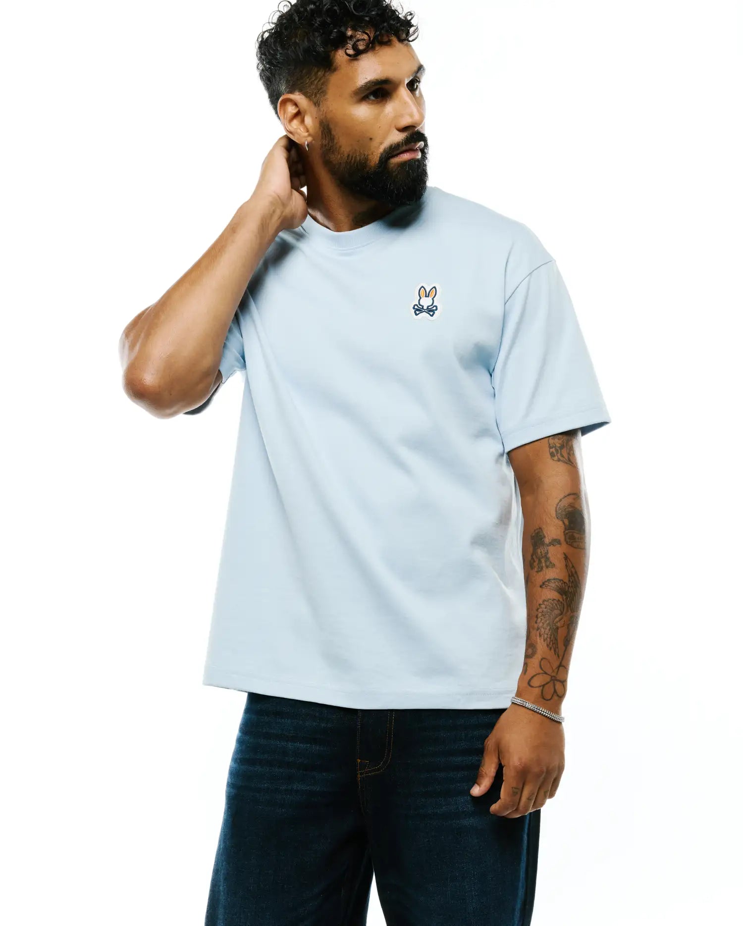 Mens Jaydon Pima Cotton Oversized-Fit Tee in light blue, featuring a small embroidered orange, navy, and white Psycho Bunny skull logo on the left chest. Smooth Pima cotton jersey texture.