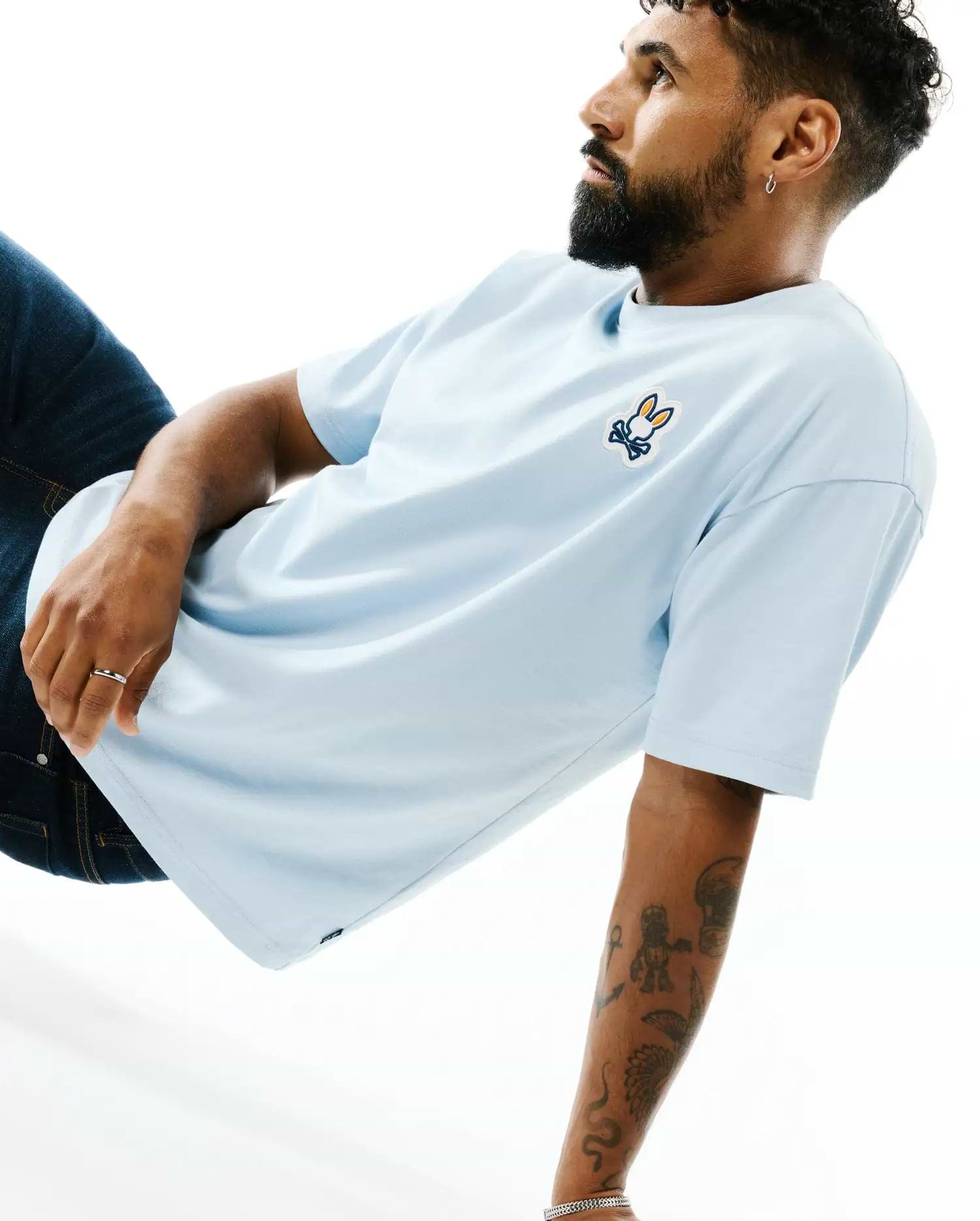 Mens Jaydon Pima Cotton Oversized-Fit Tee in light blue, featuring a smooth jersey texture and a vibrant orange, white, and blue embroidered Psycho Bunny skull logo on the left chest.
