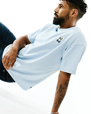 Mens Jaydon Pima Cotton Oversized-Fit Tee in light blue, featuring a smooth jersey texture and a vibrant orange, white, and blue embroidered Psycho Bunny skull logo on the left chest.