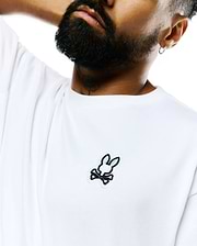 Mens Jaydon Pima Cotton Oversized-Fit Tee in crisp white, featuring a smooth jersey texture and a prominent embroidered Psycho Bunny skull logo with black outline and light green ears on the left chest.