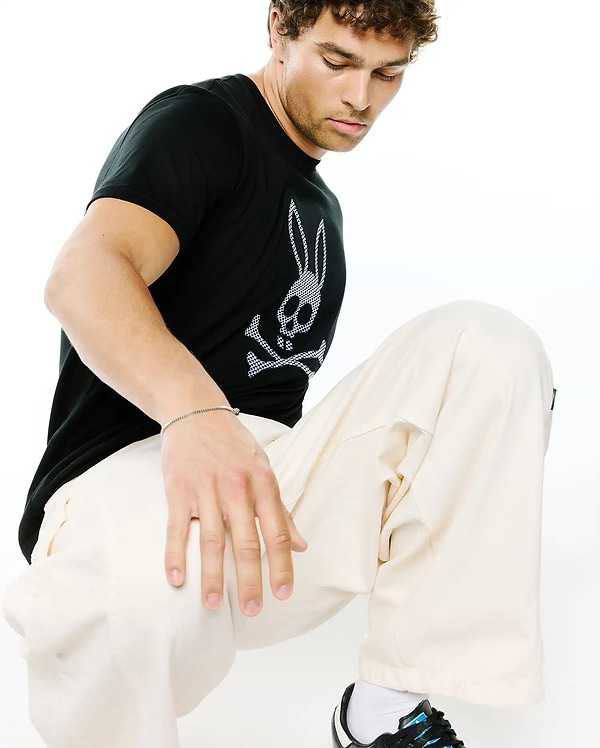Mens Stan Graphic Tee, a black classic fit soft jersey t-shirt featuring a prominent white and black checkered Psycho Bunny skull logo graphic on the chest, embodying refined streetwear.